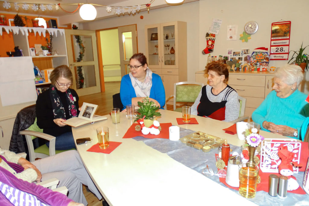 Ehrenamtliche lesen Seniorinnen vor.