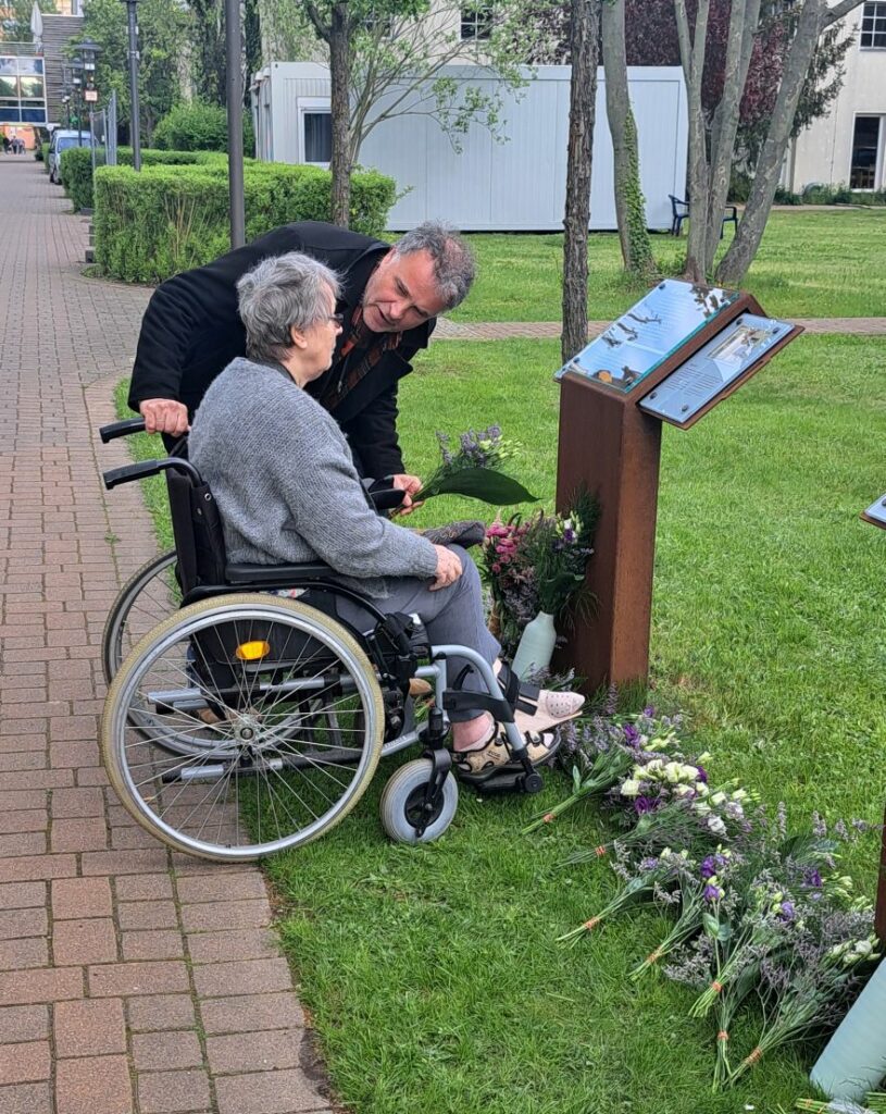 Nutzer*in legt Blumen nieder an den Gedenkstelen